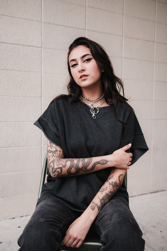Stylish woman sitting against a wall showcasing grunge fashion and tattoos.