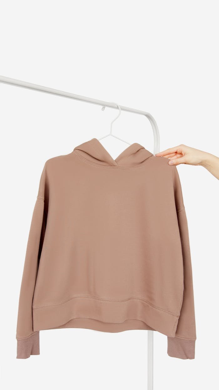 Brown hoodie on hanger with hand, ideal for apparel mockup and fashion design.